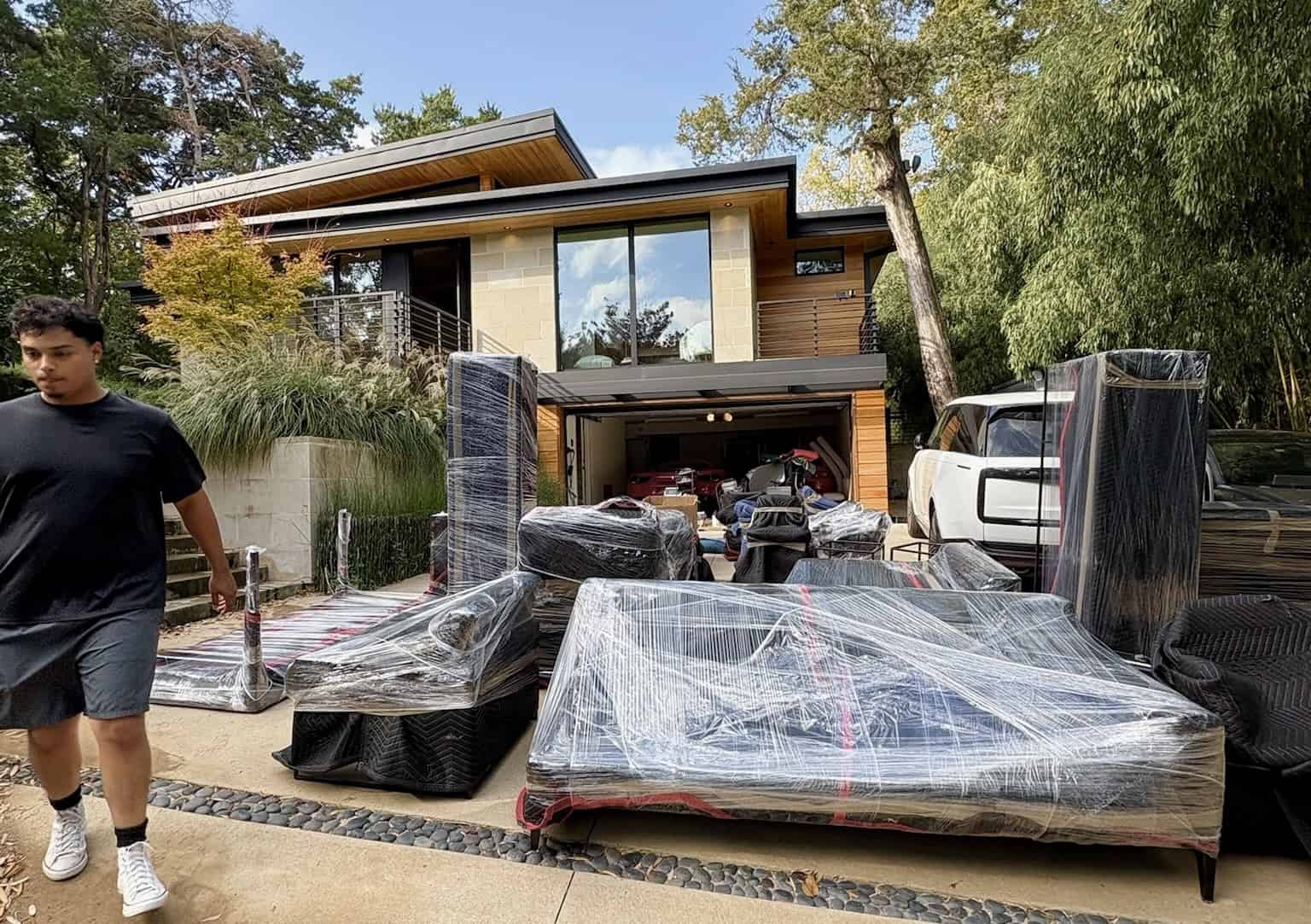 Furniture items professionally wrapped with moving blankets and stretch wrap placed in the driveway of a home after being unloaded